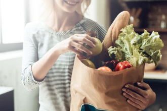 A woman collecting her groceries from a paper back with bread and lettuce sticking out on top