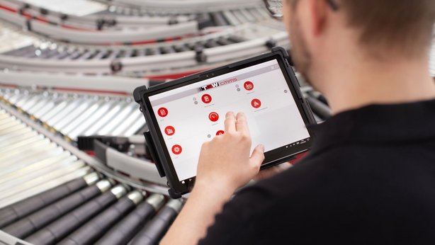TGW employee working on the Warehouse Management System on his tablet with a conveyor belt in the background
