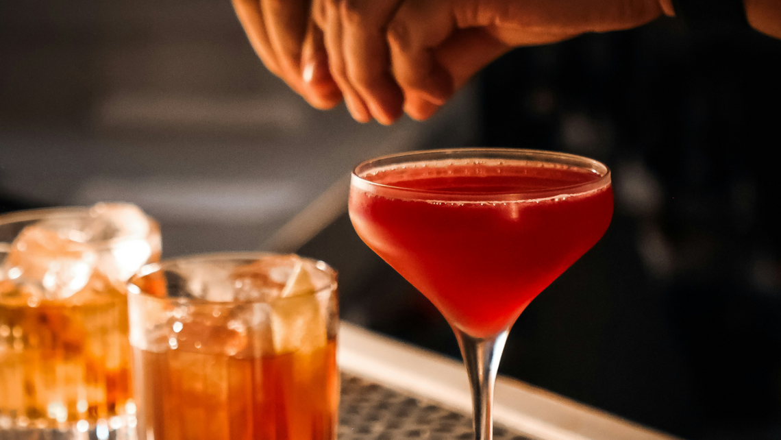 Close-up of a bartender finishing a garnish on a cocktail with two other drinks next to it in a restaurant