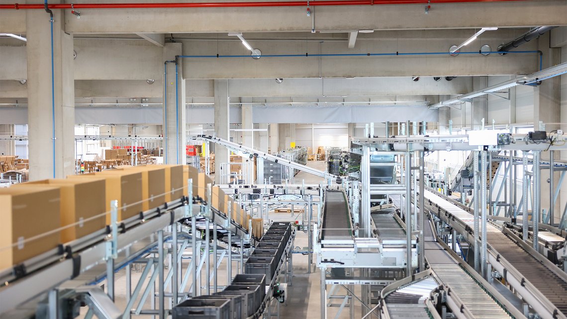 An overview of a warehouse automation system designed by TGW Logistics with pieces of conveyor belt, pickstations and rackings