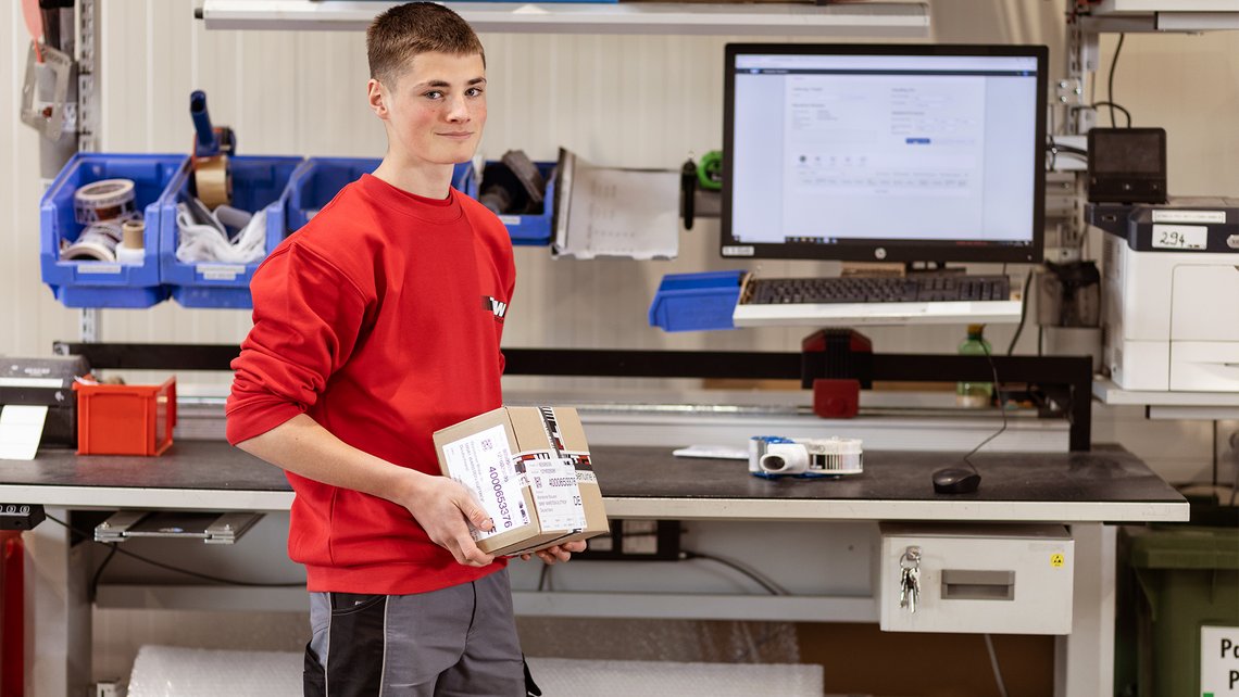 A TGW Logistics apprentice standing in front of a working station with a big desktop screen