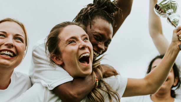 Women's athletic team in white shirts celebrating their victory by raising a trophy