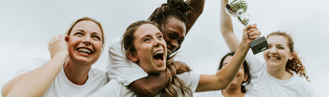 Women's athletic team in white shirts celebrating their victory by raising a trophy