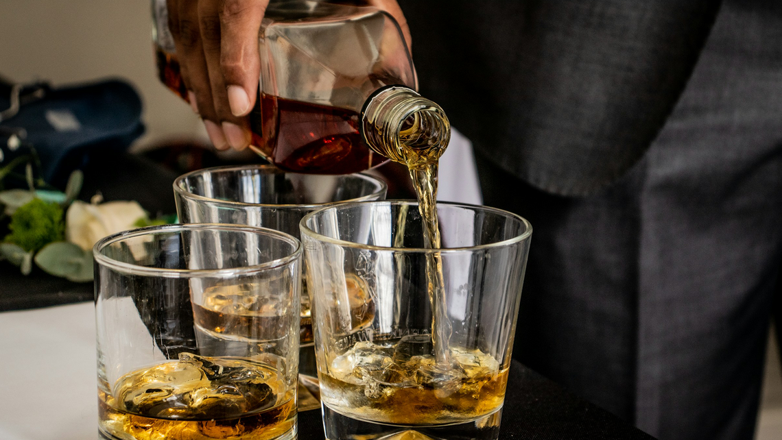 Close-up of a man in a suit pouring whiskey into three glasses