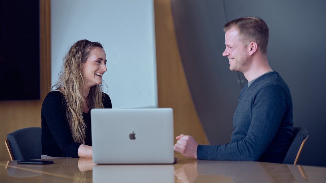 A woman and a man talking while sitting in front of a laptop
