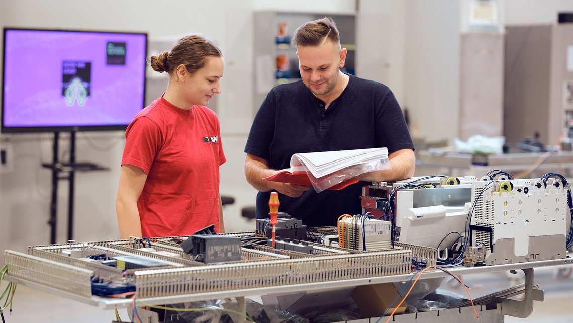 A TGW Logistics apprentice receiving an explanation about intralogistics systems by a senior employee