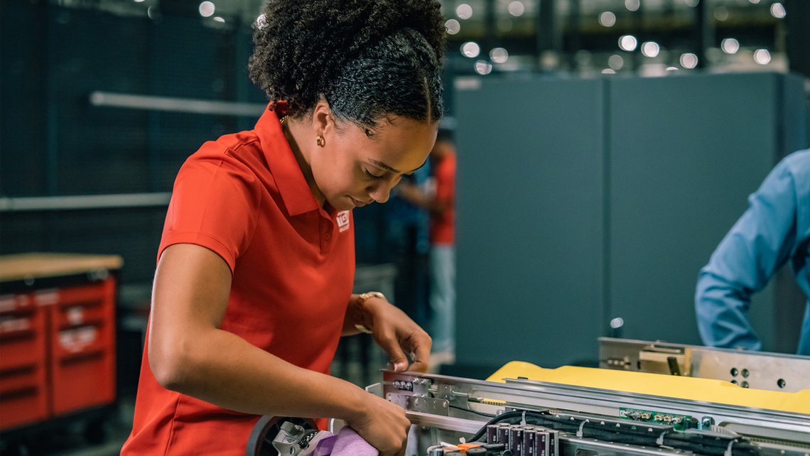 TGW Logistics employee in a red polo cleaning a Stingray shuttle
