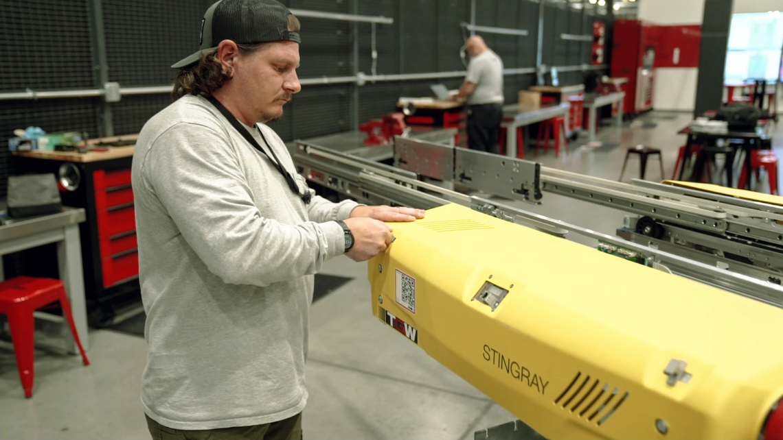 TGW Logistics Lifetime Services on-site team member inspecting and cleaning a Stingray shuttle