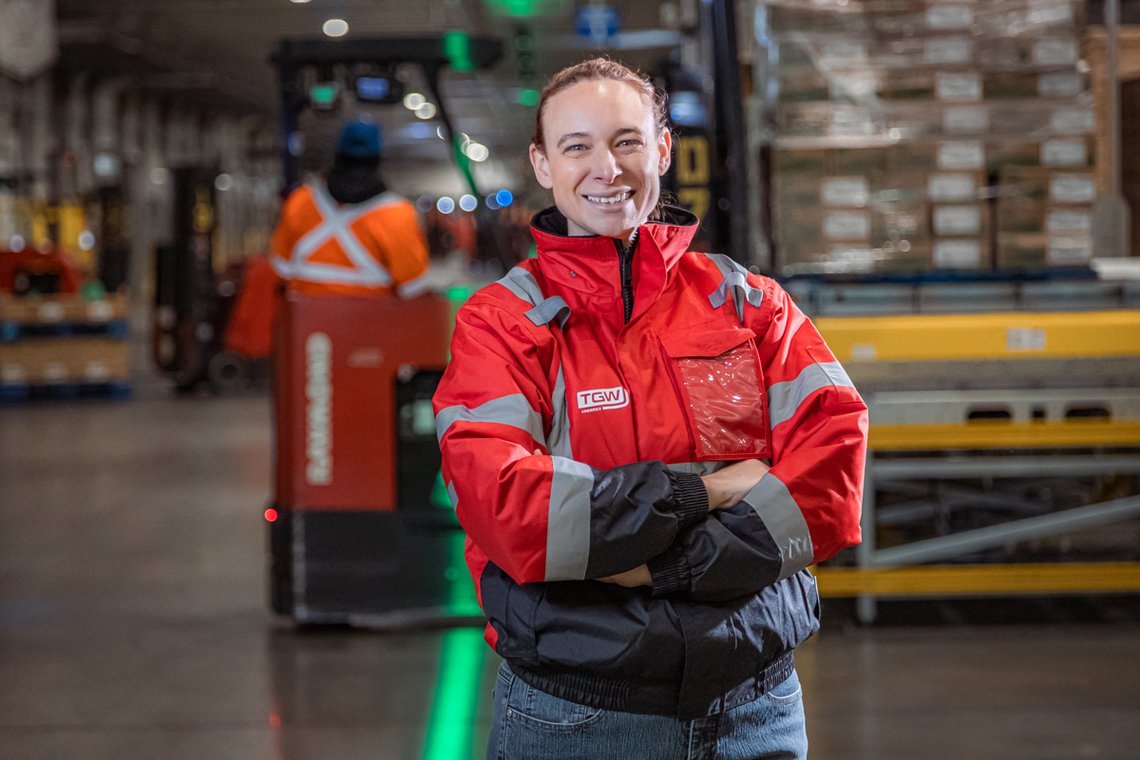 TGW Logistics employee standing in an automated cold chain facility, wearing a red jacket
