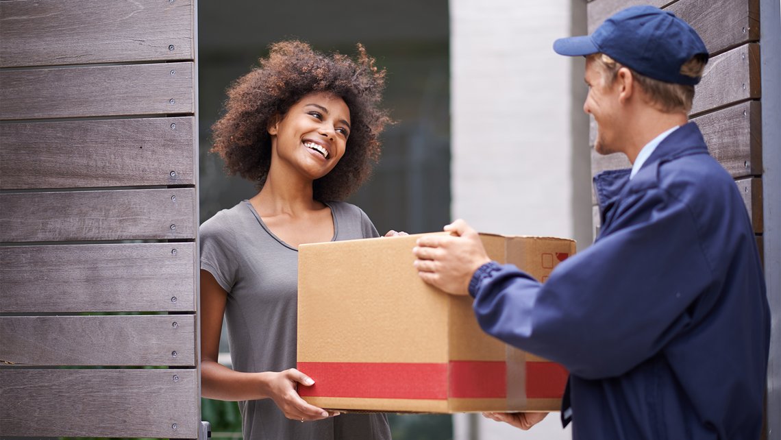 A postman delivers a large cardboard box to a woman at the door