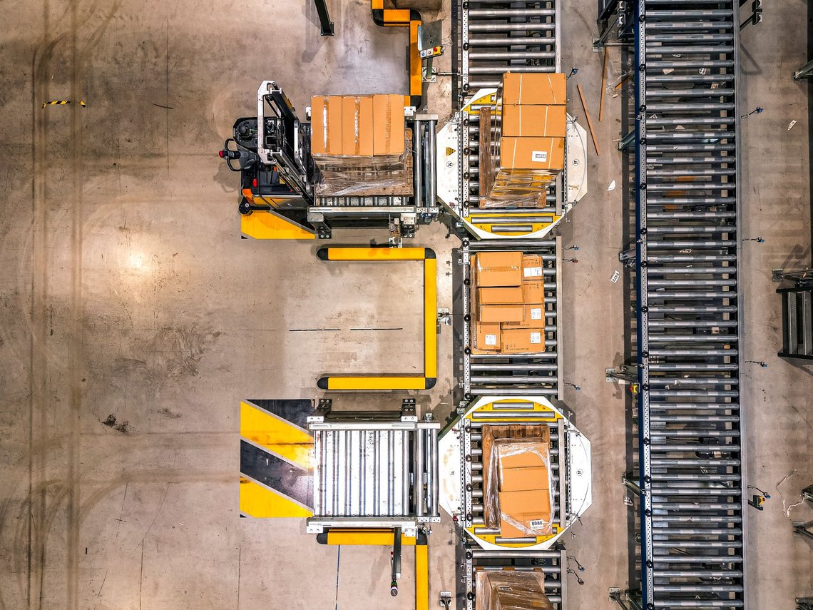 Overview of an automated warehouse where cartons are being placed from forklifts on conveyor belts.