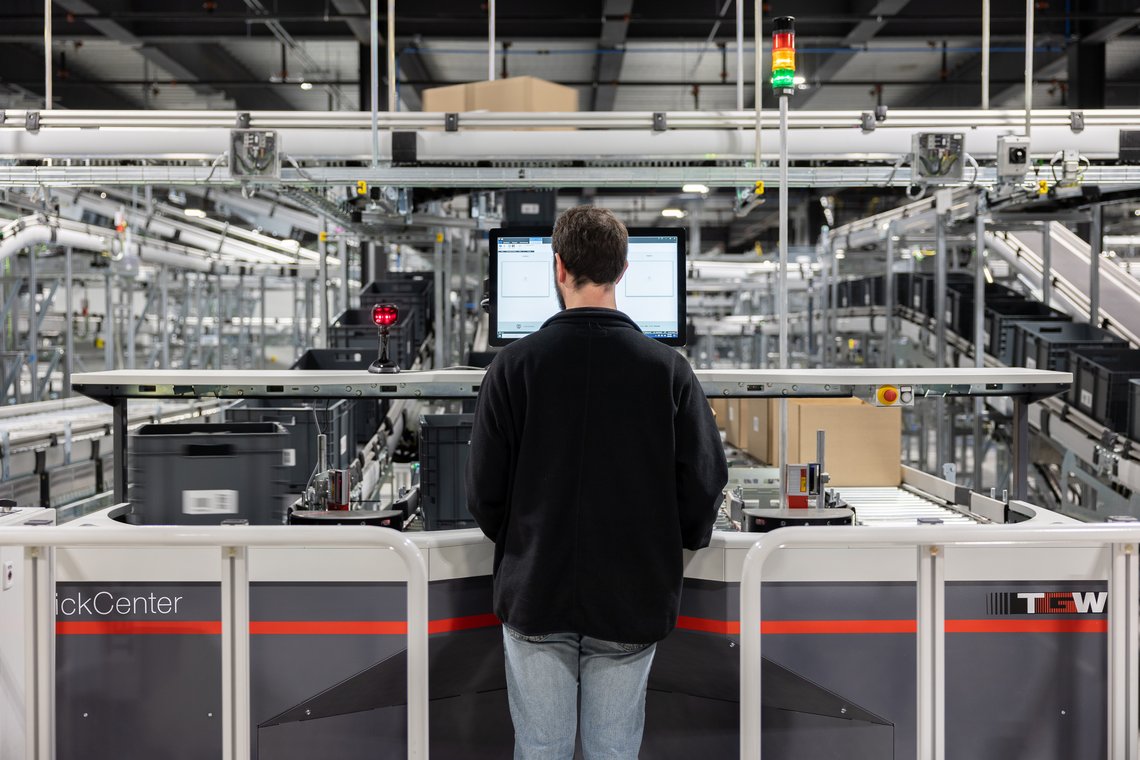 Warehouse worker picking from a tote into a pre-made box at a TGW Logistics PickCenter One picking station