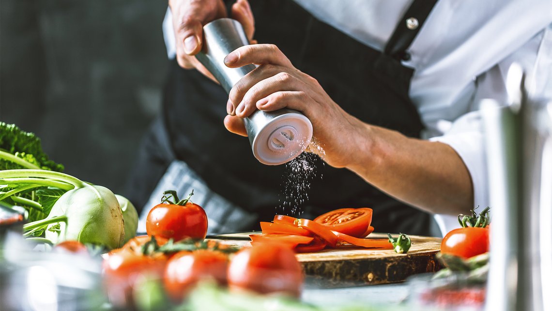 A chef salting tomatoes on a cutting board