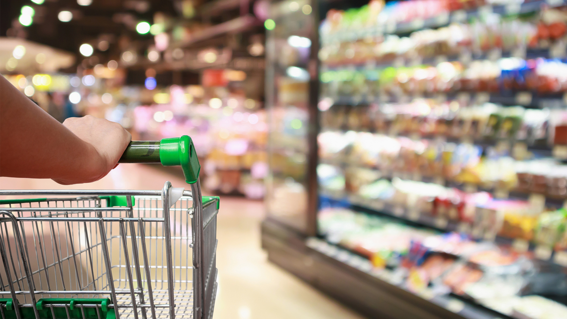 Grocery cart going through a refrigerated goods aisle in the grocery store