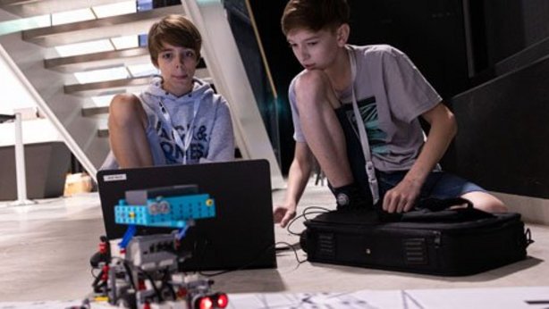 Two young people playing with a small robot they designed themselves. They are participating in the TGW Logistics RoboChallenge