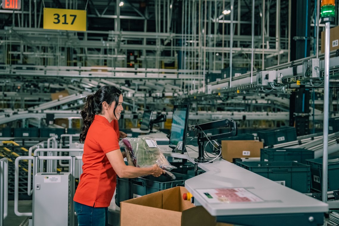 Warehouse worker picking from a tote into a pre-made box at a TGW Logistics PickCenter One picking station