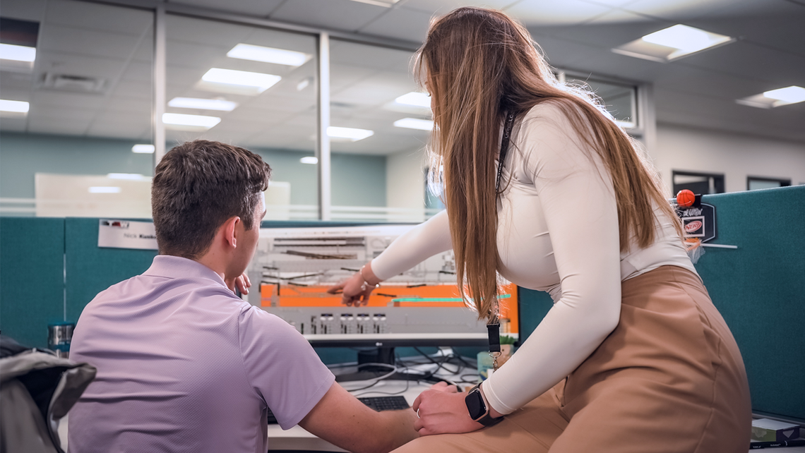 Two TGW Logistics' employees looking at a computer screen and problem solving together