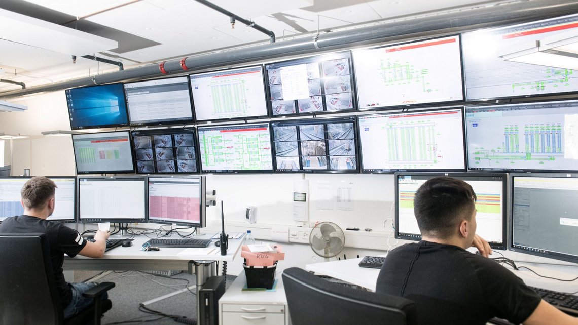 [Translate to North America:] Two persons in front of a large number of screens
