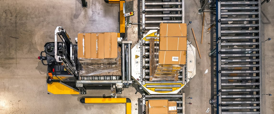 Overview of an automated warehouse where cartons are being placed from forklifts on conveyor belts.