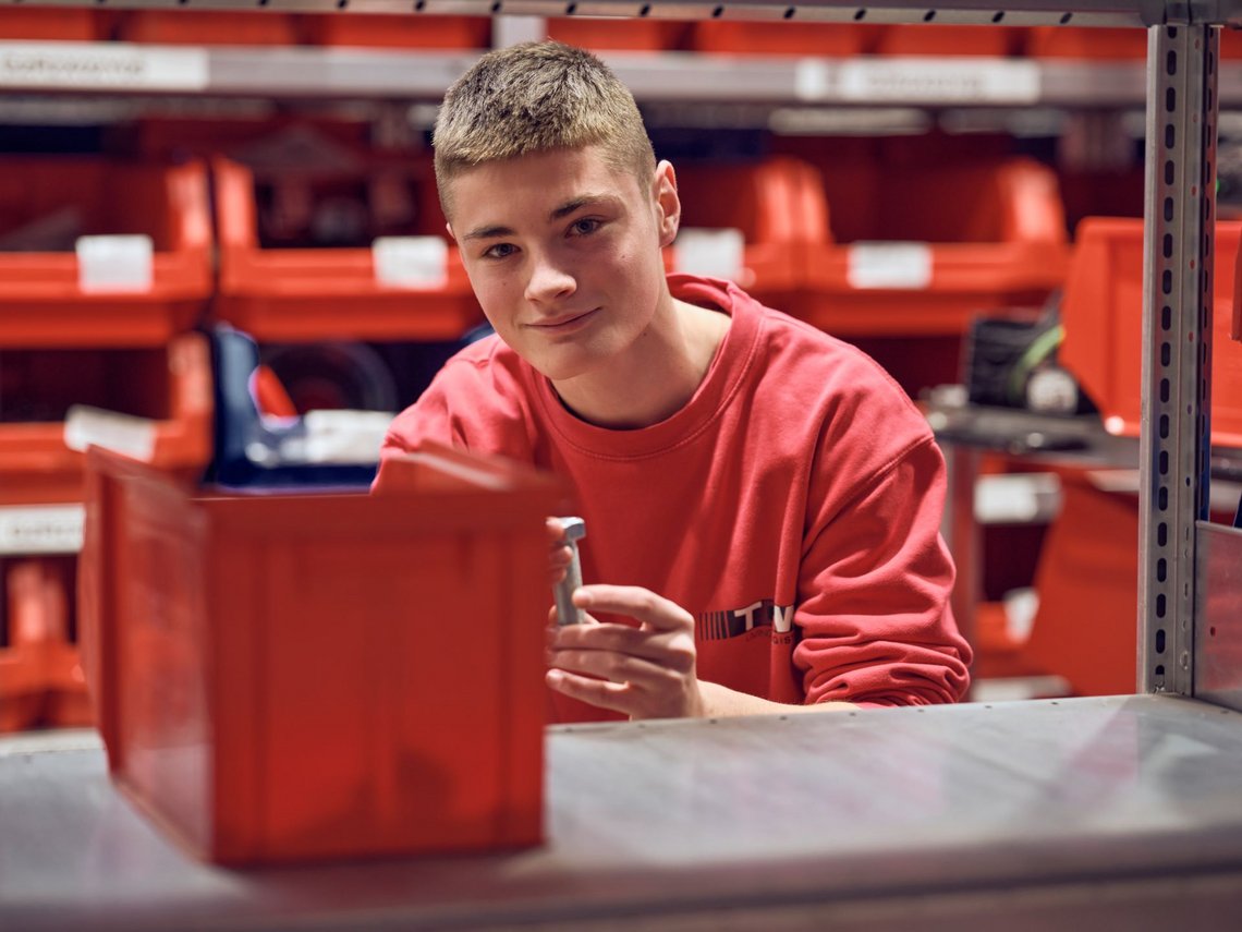 [Translate to France:] A TGW service employee smiles into the camera, holding a tablet in his hand