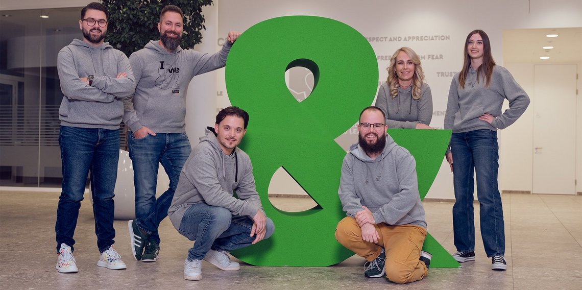 A team picture with the big &-sign at the entrance of the TGW Headquarters