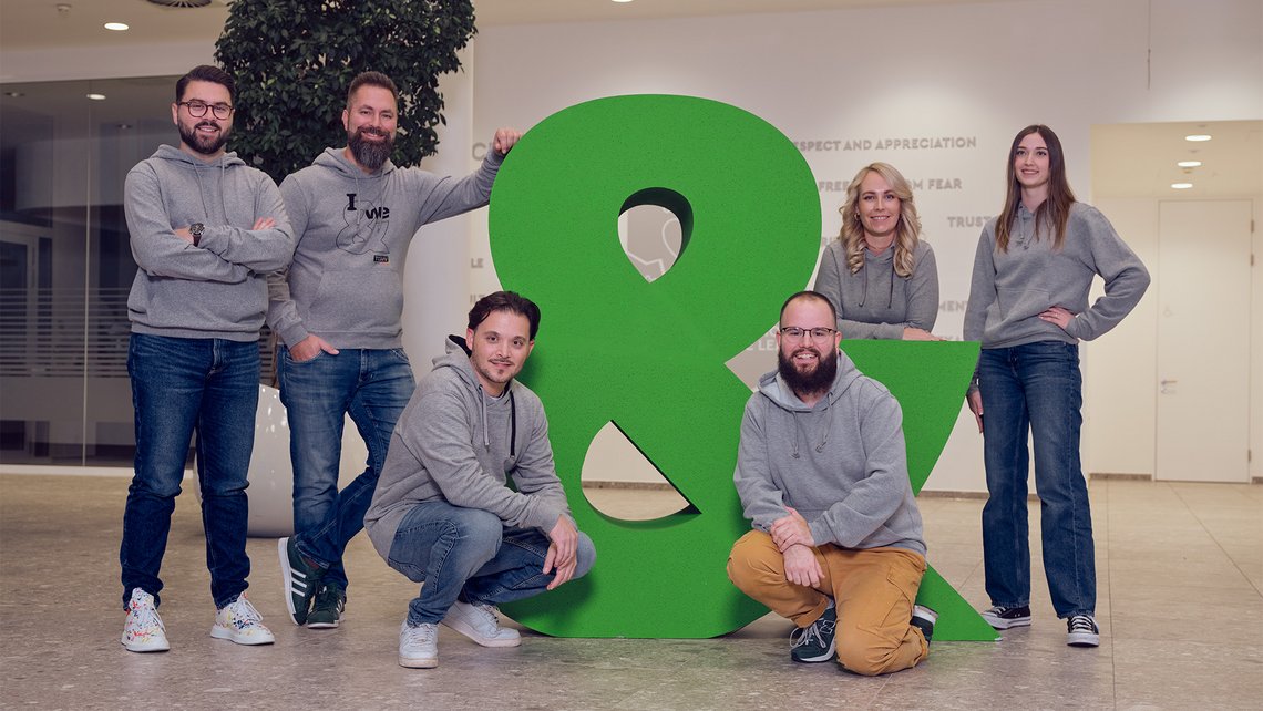 A team picture with the big &-sign at the entrance of the TGW Headquarters