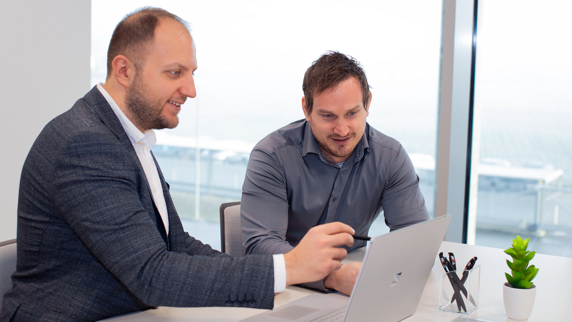 Two men looking at a touchscreen laptop, discussing warehouse automation solutions