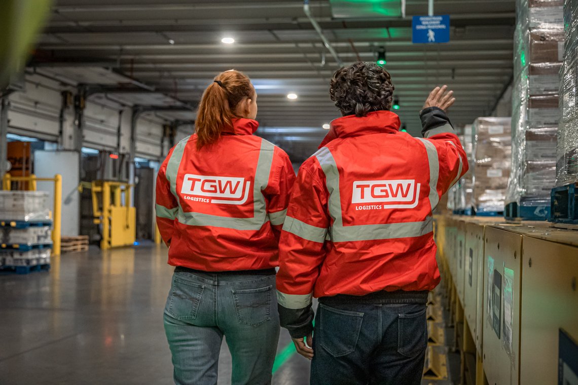 TGW Logistics employees standing and pointing in an automated cold chain facility, wearing red jackets