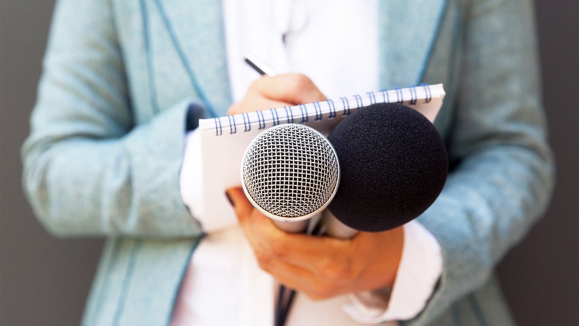 Close-up of women's hands holding two microphones and a notepad