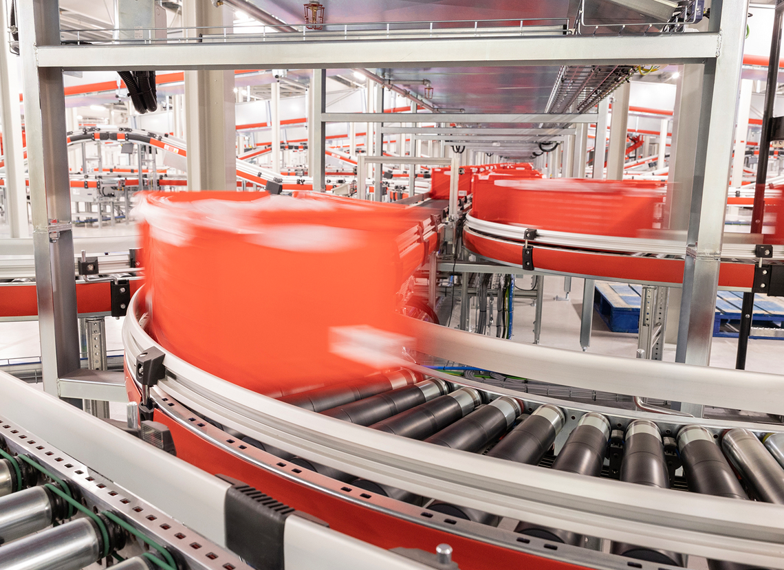 Red totes traveling on multiple conveyor systems throughout the distribution center area